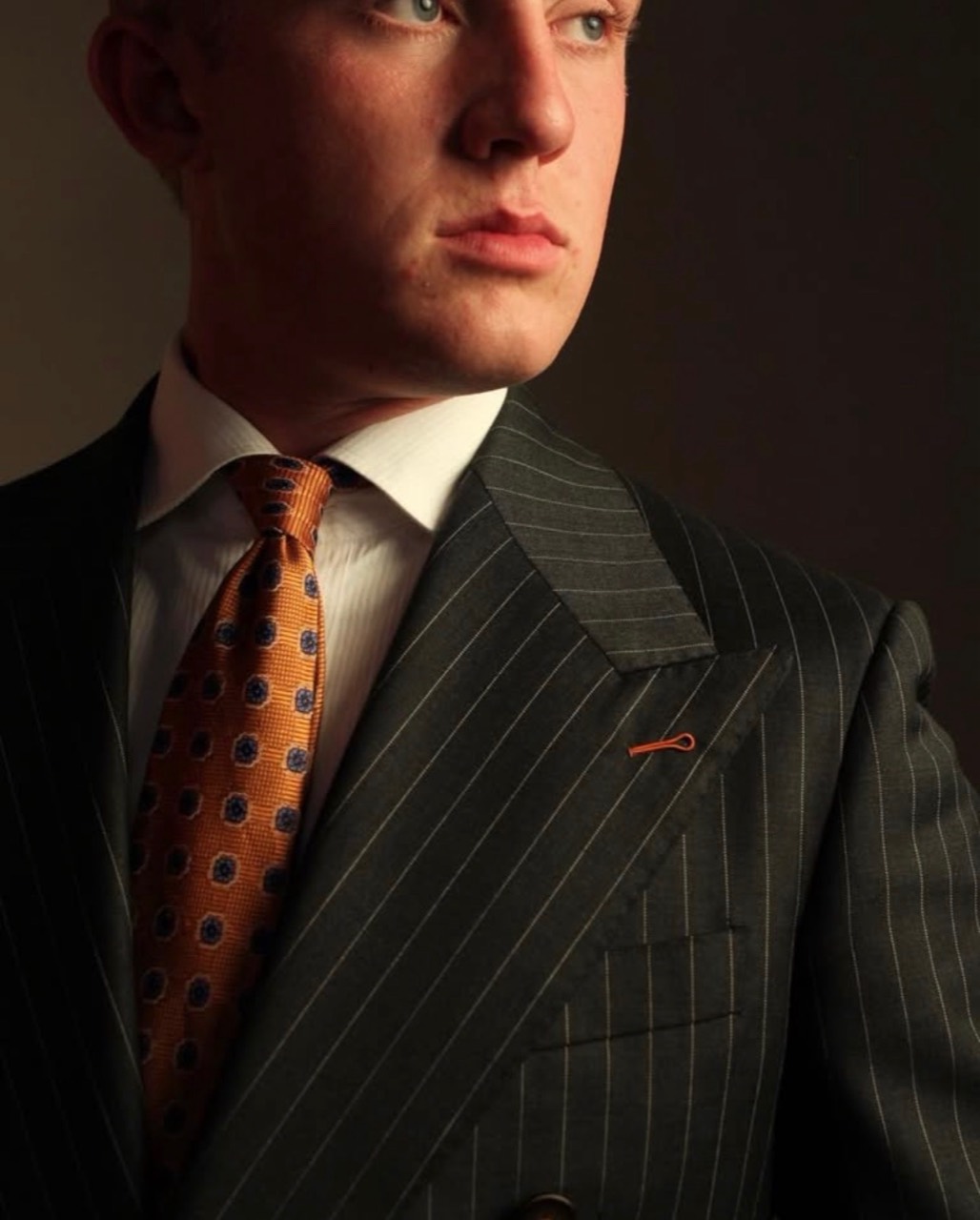 Man wearing a dark pinstripe custom suit and orange tie
