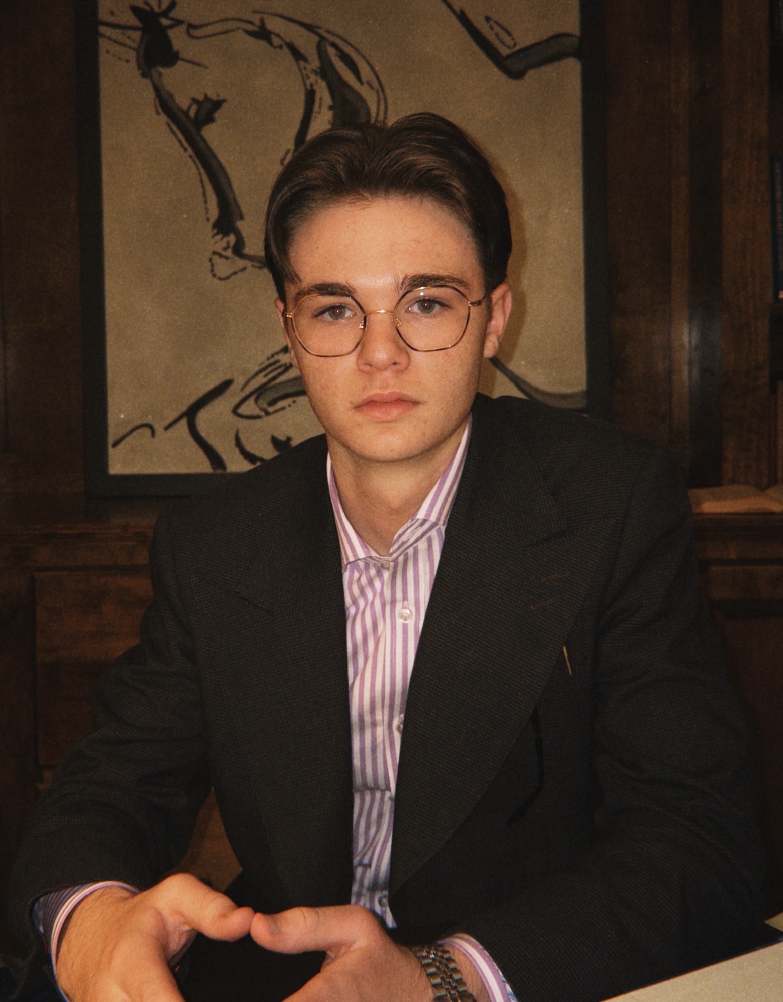 Gabriel Adams wearing glasses, a dark blazer, and a striped shirt